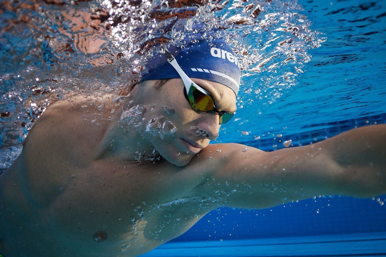 A swimmer in a navy cap and mirrored goggles swimming freestyle underwater